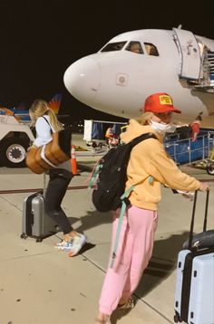 two people walking towards an airplane with luggage on the tarmac and one person wearing a face mask