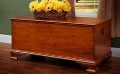 a basket with yellow flowers sits on top of a wooden chest in front of a window