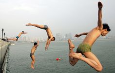 three men jumping into the water from a pier to another man in swimsuits