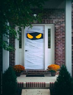 a white door with yellow eyes on it in front of some bushes and flowers outside