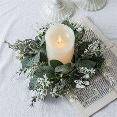 a lit candle sitting on top of a book next to some greenery and leaves