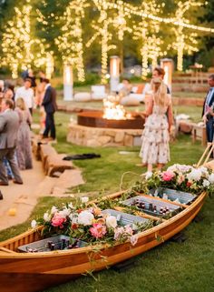 a row boat with flowers and candles on the grass in front of people standing around