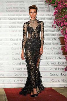 a woman in a black dress standing on a red carpet with pink flowers behind her