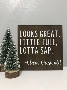 a wooden sign that says looks great, little full, lotta sapi and a small christmas tree