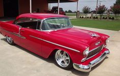 an old red car parked in front of a garage