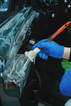 a person in blue gloves is cleaning the interior of a car with a brush and rag