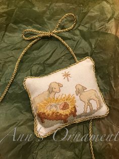 a cross stitch pillow with two sheep and a manger scene on it, tied to a green sheet