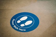 there is a sticker on the floor that says please wait here with footprints in it