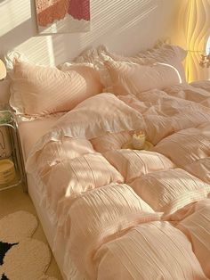 an unmade bed with pink comforter and pillows on the floor next to a window