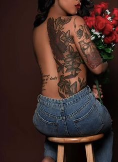 a tattooed woman sitting on a stool holding flowers