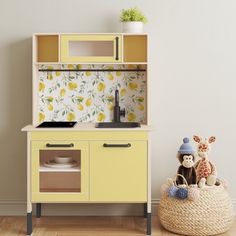 a toy kitchen with yellow cupboards and toys in the basket on the wooden floor