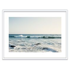 an ocean scene with waves crashing on the shore and rocks in the foreground, framed in white