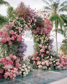 an arch made out of flowers on the side of a road with palm trees in the background