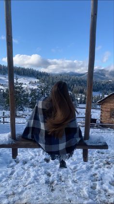 a woman sitting on a bench covered with a blanket in the snow, looking at mountains