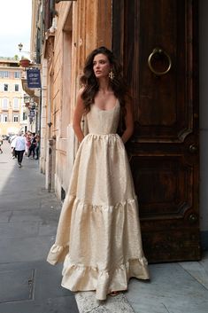 a woman standing in front of a wooden door wearing a dress with tiered ruffles