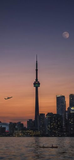 an airplane is flying over the city at night with a full moon in the sky