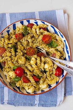 a bowl filled with pasta and vegetables on top of a blue and white striped napkin