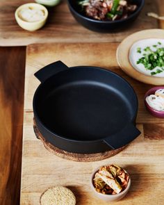 a wooden cutting board topped with two black pans filled with food