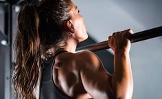 a woman with long hair holding a barbell in her right hand and looking up at the sky