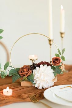 flowers and candles on a wooden table with white plates, napkins and silverware