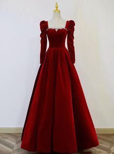 With this prom dress, the evening becomes an event of regal splendor. The gown's deep red velvet is a striking statement of both passion and refinement, while its fitted bodice, embellished with an intricate pattern of crystals, shines with an understated elegance. The puffed sleeves, a nod to the romantic styles of yesteryear, frame the arms with a dramatic poise, and the sweeping skirt creates a silhouette that is both commanding and graceful. This dress is an invitation to step into a world of sophistication and to embrace a night of unforgettable memories, all while draped in the epitome of prom perfection. Red White Prom Dress, Red Winter Wedding Dress, Royal Night Gown, Plain Net Gown Designs Latest, Red Gown With Sleeves, Red Masquerade Dress, Velvet Gowns Evening Dresses, Red Suits For Women, Velvet Gown Design