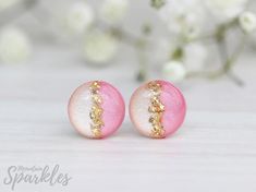 two pink and white earrings with gold sparkles on them, sitting next to flowers