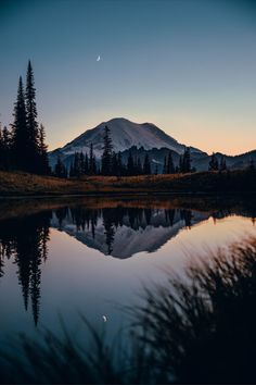 a mountain is reflected in the water at sunset with trees and grass on the shore