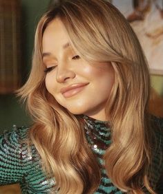 a close up of a woman with long blonde hair and wearing a green top smiling at the camera