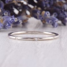 a white gold wedding band with three diamonds on it and purple flowers in the background