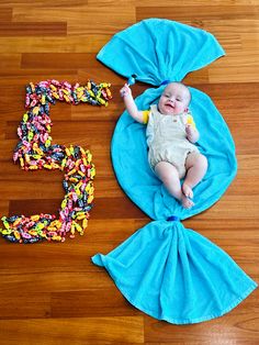 a baby laying on top of a blue blanket next to the numbers 5 and 5