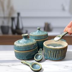 a hand is holding a spoon over some ceramic dishes