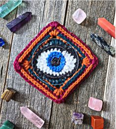 a crocheted square with an eye in the center surrounded by crystals on a wooden surface