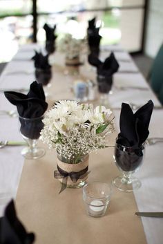 the table is set with black napkins and white flowers in vases on it