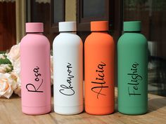 three different colored water bottles sitting next to each other on top of a wooden table