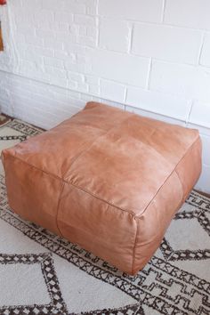 a brown leather ottoman sitting on top of a rug