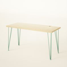 a wooden table with green hairpinks on the legs and a white wall in the background