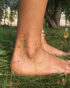 a close up of a person's bare foot with flowers on the grass and trees in the background