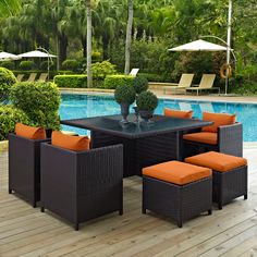 an outdoor dining table with orange cushions next to a swimming pool