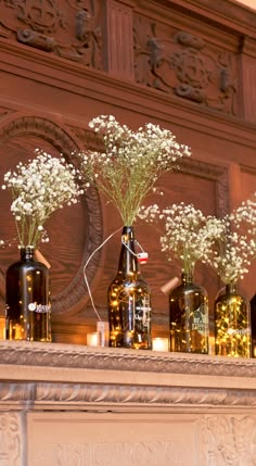 flowers are in vases sitting on the mantel above a mantle with candles and bottles