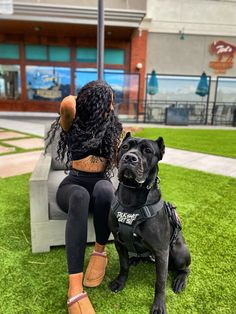 a woman sitting on top of a bench next to a black dog in front of a building