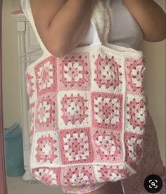 a woman holding a pink and white crocheted bag in front of her face