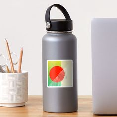 a stainless steel water bottle next to a white laptop and pencils on a wooden table