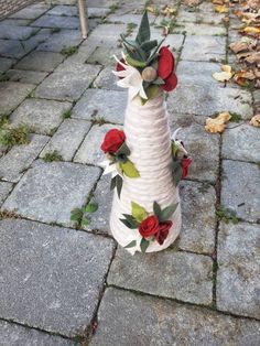 a white vase sitting on top of a stone walkway covered in red flowers and greenery