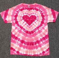 a pink and red tie - dyed shirt with a heart on the front, sitting on a carpeted floor