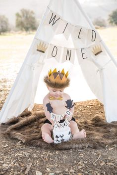 a baby wearing a crown sitting in front of a teepee