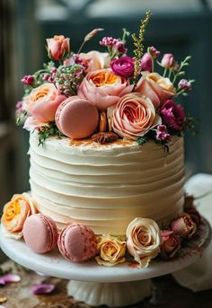 a white cake with flowers and macaroons on the top is sitting on a table