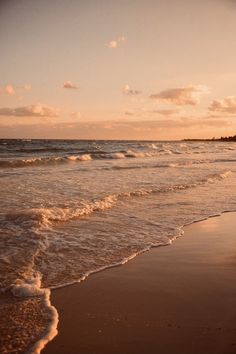 an ocean beach with waves coming in to shore and the sun setting on the horizon