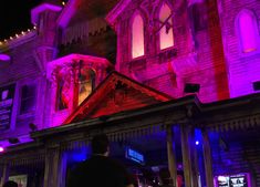 people are standing in front of a building lit up with purple and red lights at night