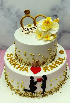 a white cake with gold decorations and two people holding hands in front of the cake