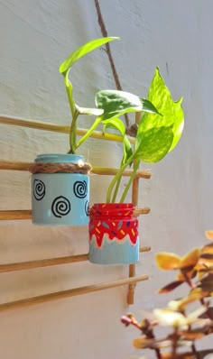 two vases with plants in them are hanging on a wooden rack against the wall